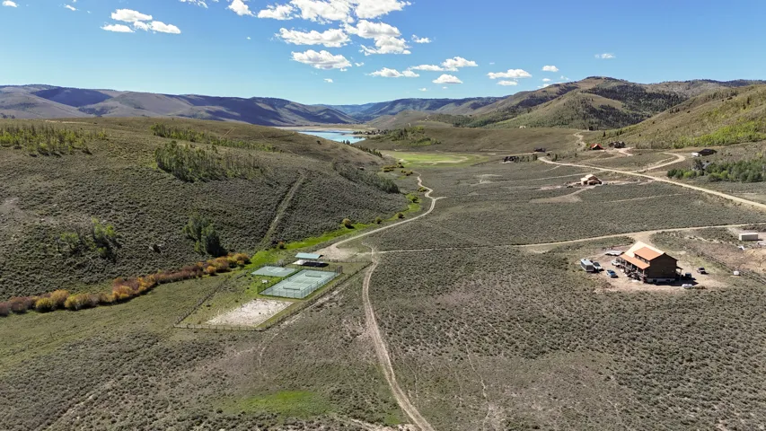 Expansive property featuring rugged terrain, a distant body of water, several structures, a tennis court, and a riverbed