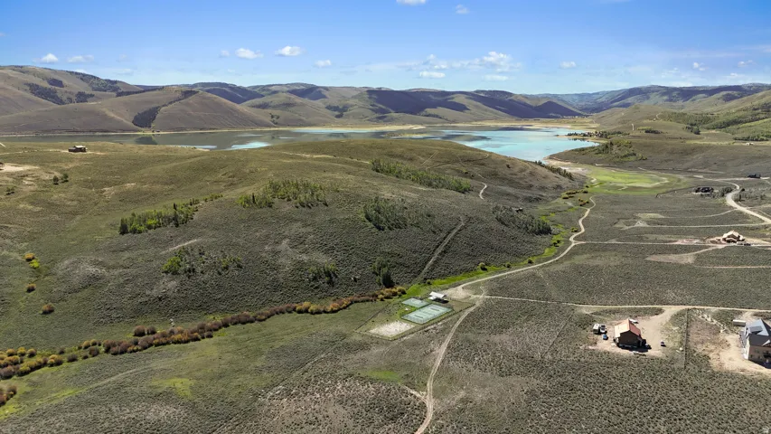 Expansive land parcel featuring a visible tennis court, a lake, and surrounding mountains