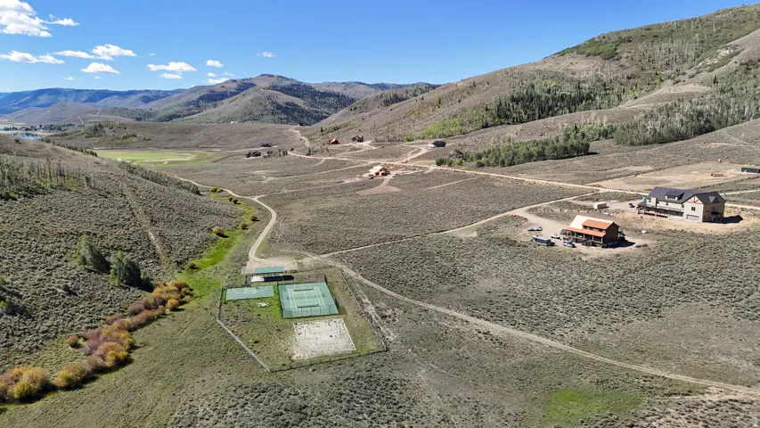 Expansive land parcel featuring multiple residential structures, a tennis court, and a volleyball court, all set amidst rolling hills and distant mountains