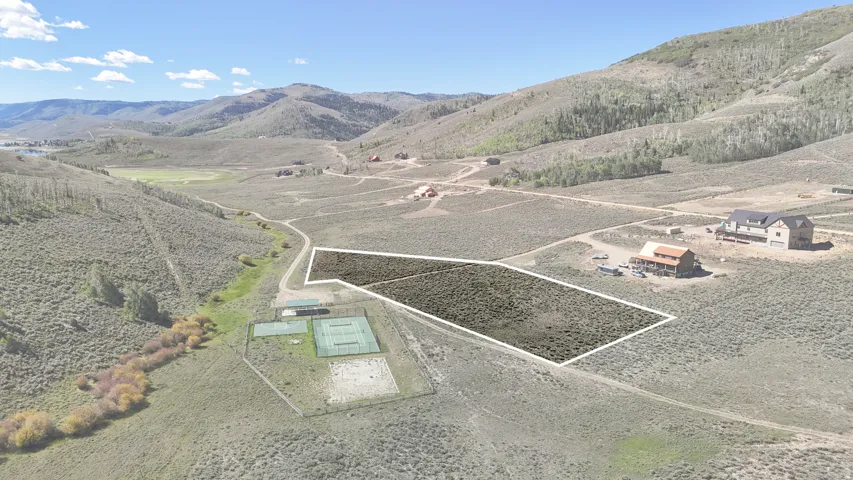 Expansive land parcel with surrounding mountain terrain, featuring a nearby tennis court structure
