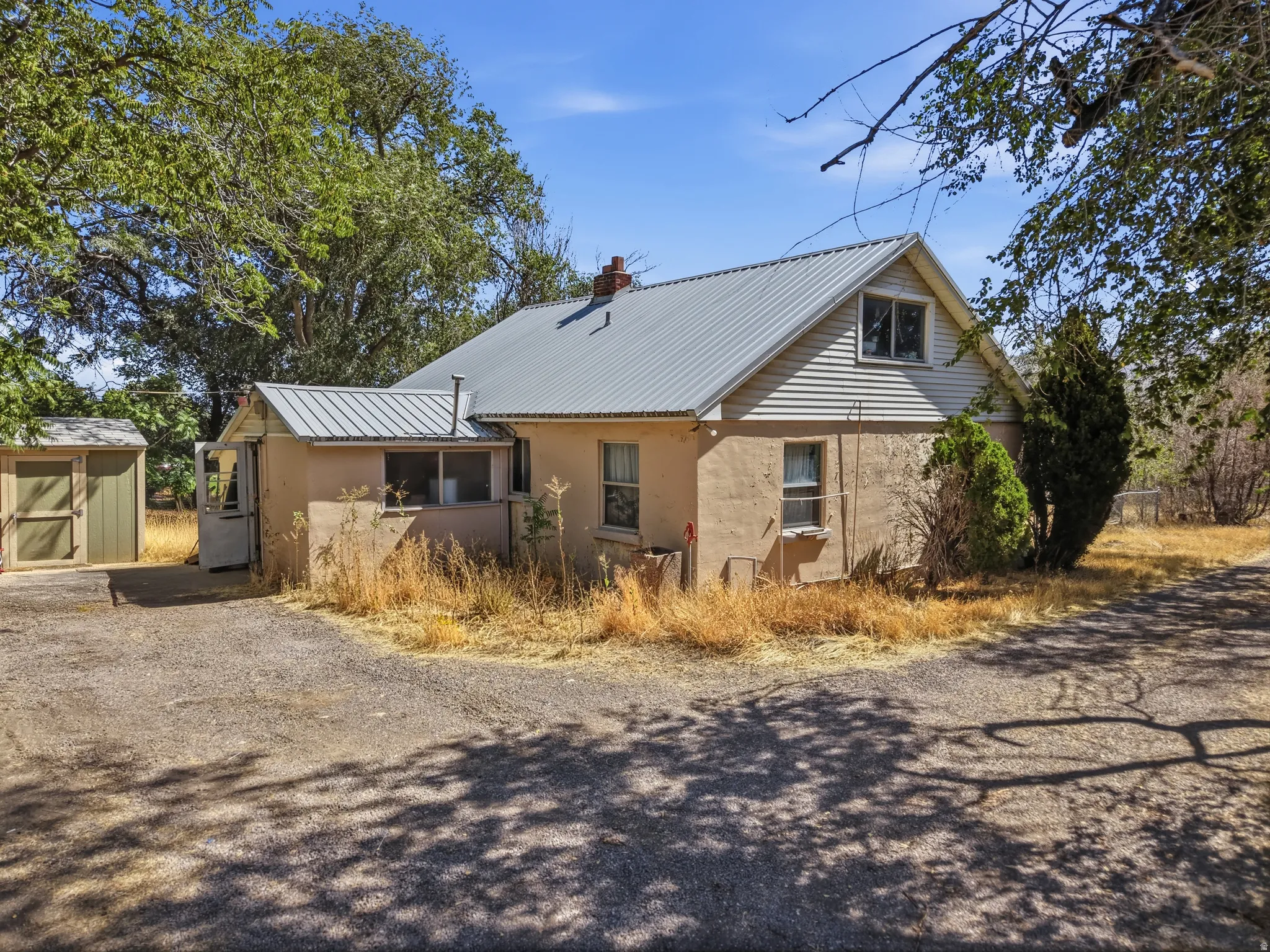 Stucco exterior with a metal roof, featuring an attached screened-in porch and an additional shed