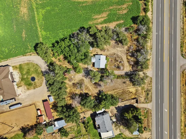 Expansive land featuring a single-story dwelling, mature trees, and direct road access