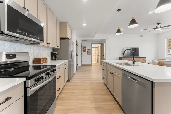 Modern kitchen featuring light wood-finish flooring, light-toned cabinetry with dark hardware, stainless steel appliances, white countertops, and a full-height tile backsplash