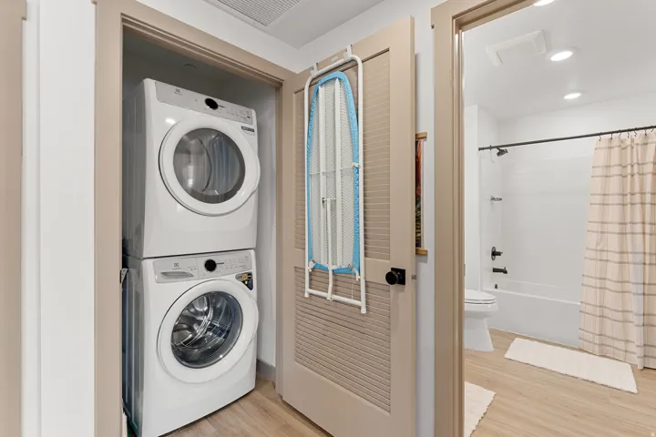 Stackable washer and dryer, wood-finish flooring, white tiled shower, recessed lighting, and a louvered door