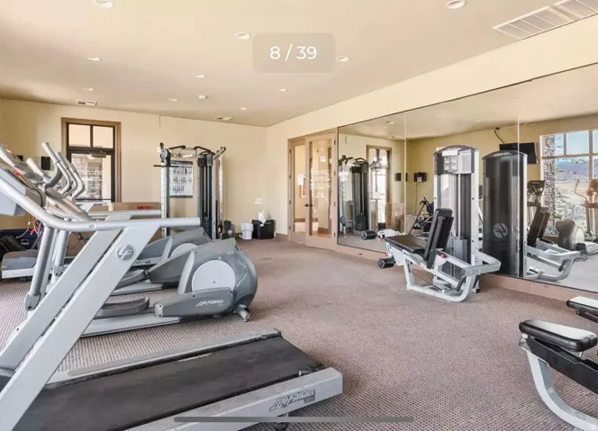 Recessed lighting illuminates this fitness space, featuring wall-mounted mirrors and carpet flooring
