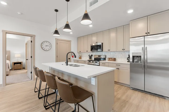 Kitchen island with a white countertop and built-in sink, stainless steel appliances, light-toned cabinetry with dark hardware, a herringbone pattern tile backsplash, and wood-finish flooring