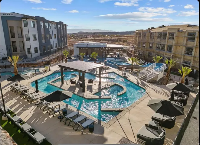 Resort-style pool area featuring a lazy river, multiple lounge seating areas, and a covered pergola