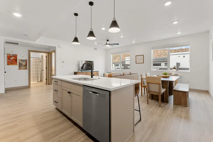 Spacious open-concept living area featuring light wood-finish flooring, recessed lighting, and a modern kitchen island with an integrated sink and dishwasher