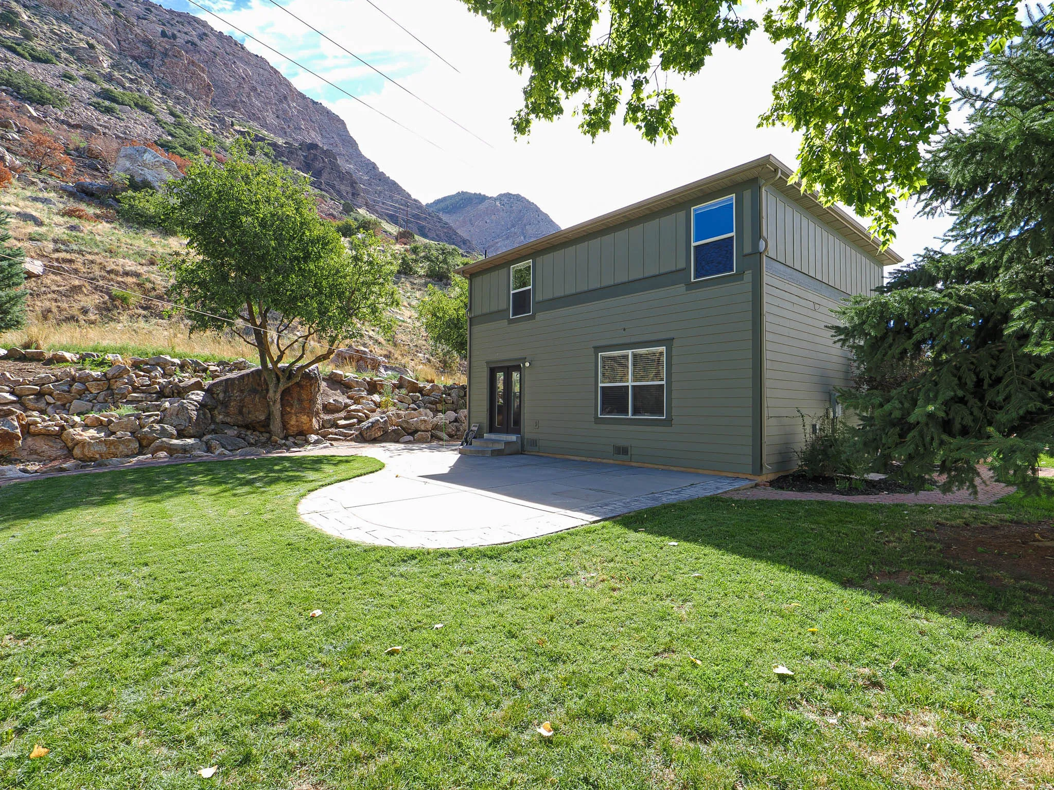 Expansive green lawn with a curved concrete patio, bordered by a stone retaining wall