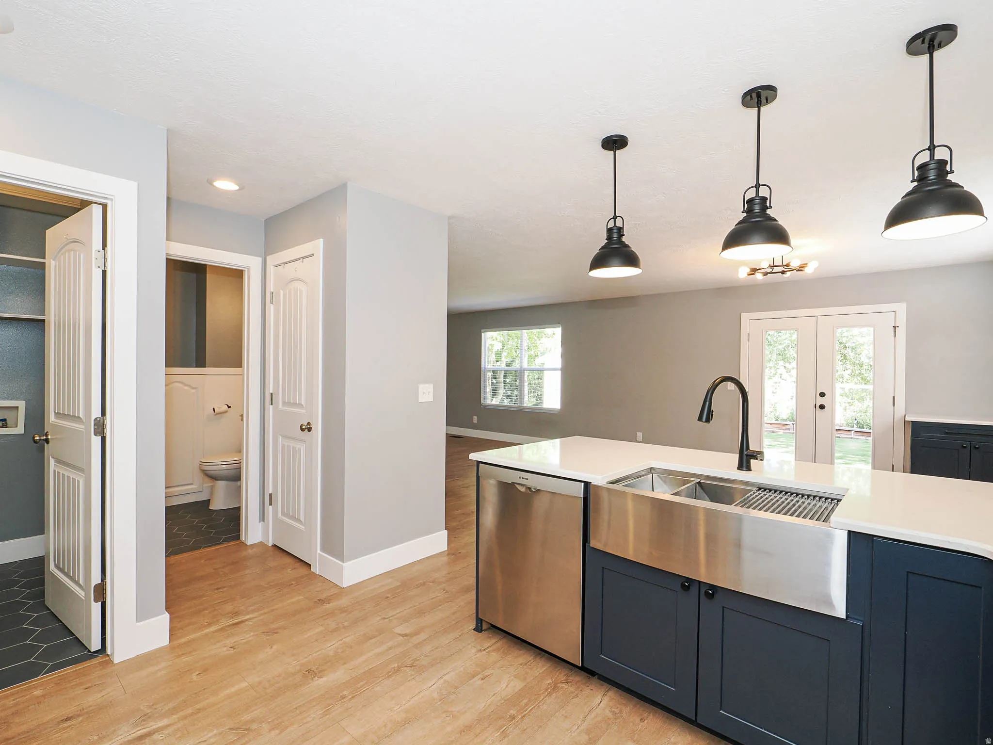 Kitchen island featuring a farmhouse sink, stainless steel dishwasher, and pendant lighting