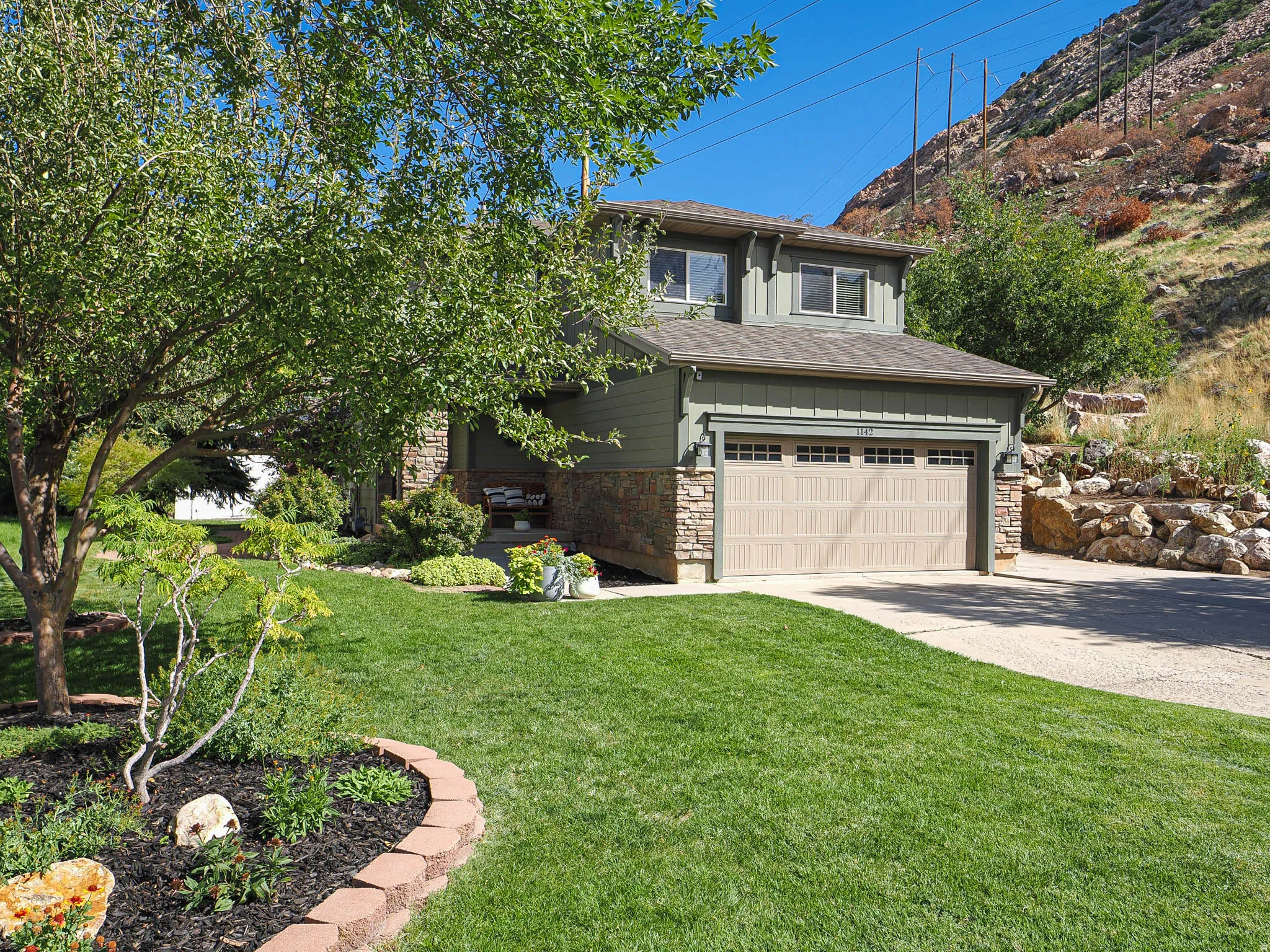 Stone and siding exterior with a light-colored garage door, complemented by a concrete driveway and a manicured lawn