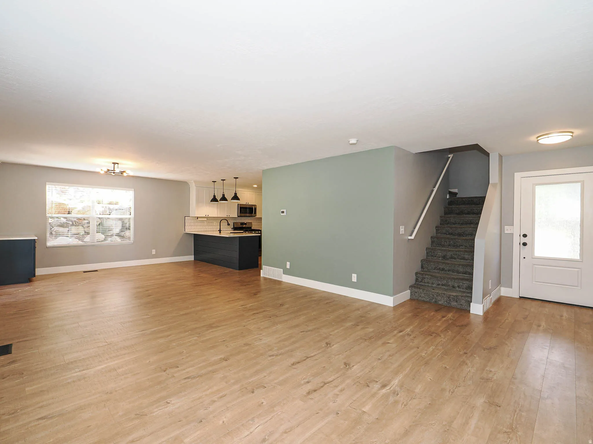 Wood-finish flooring throughout, modern kitchen with dark cabinetry and pendant lighting, built-in staircase, and a white entry door with frosted glass