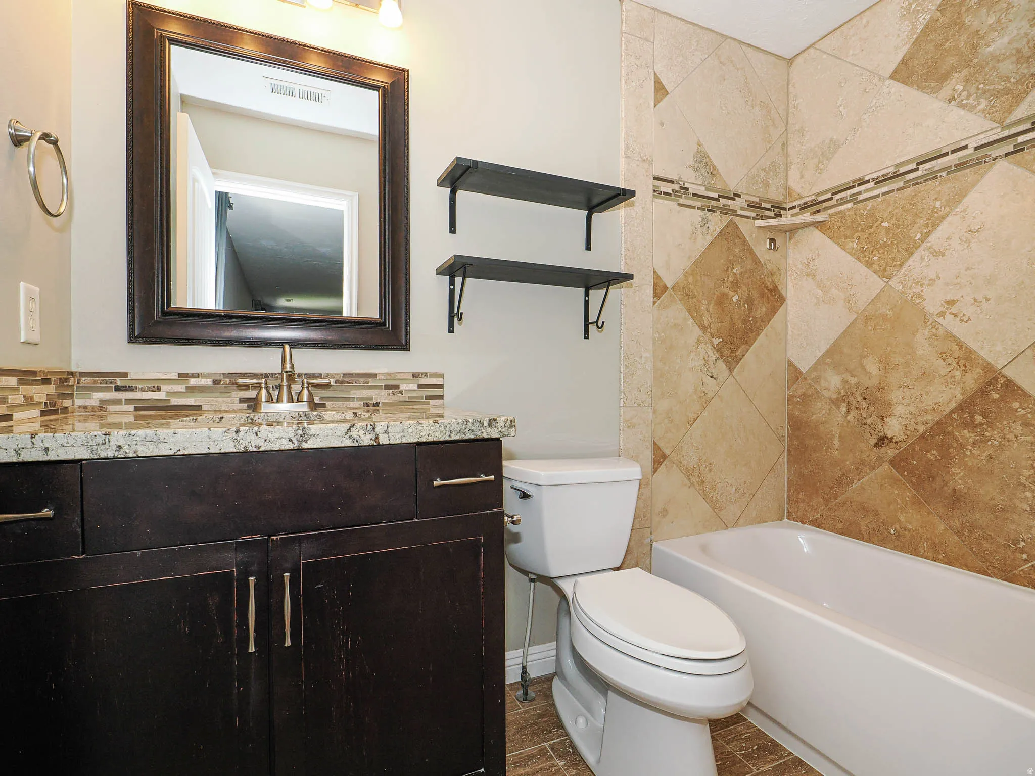Dark wood-finish vanity with a light-toned countertop, mosaic tile backsplash, and coordinating floor tile