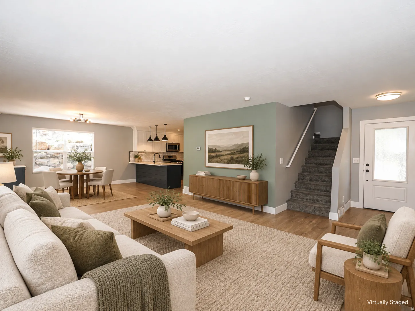 Open-concept living area with wood-finish flooring, a kitchen island with pendant lighting, a dining area with a chandelier, and a carpeted staircase