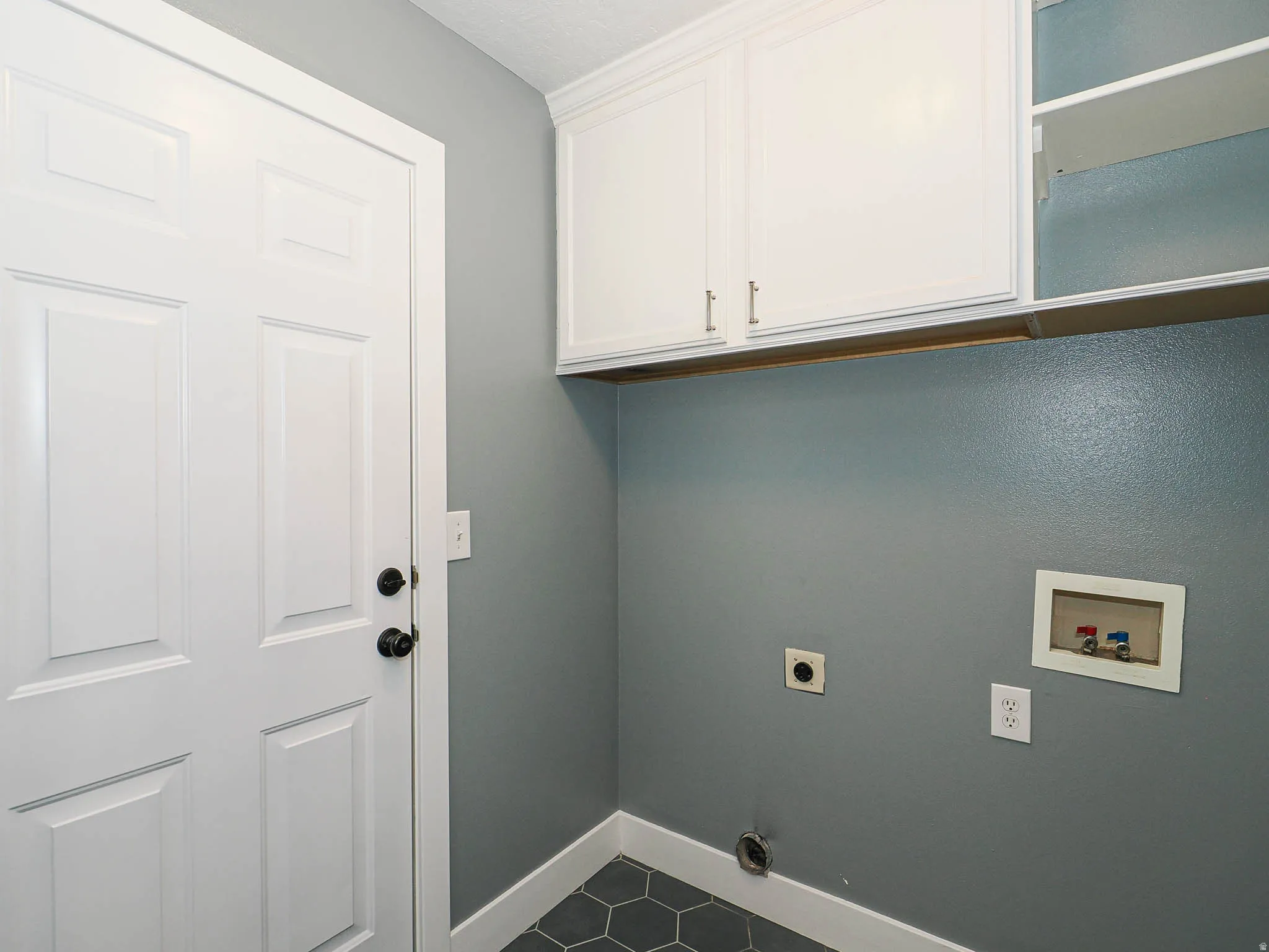 White paneled door with black hardware, white upper cabinetry, open shelving, and hexagonal floor tile