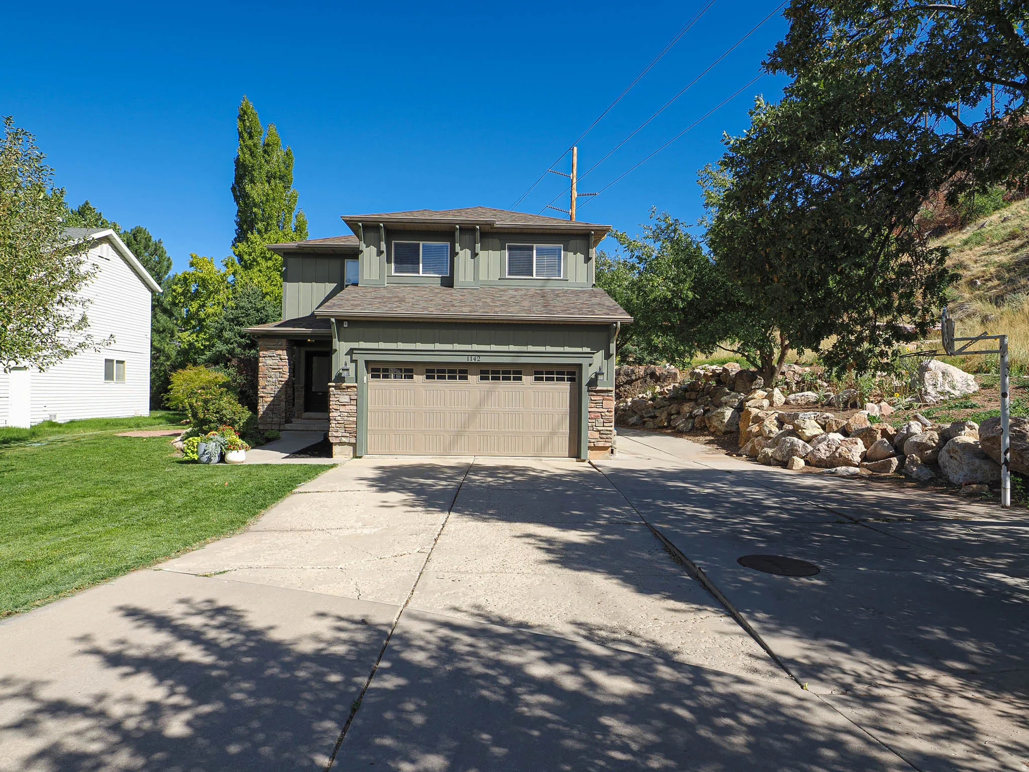 Two-story residence featuring a two-car garage, stone and siding exterior, and a concrete driveway