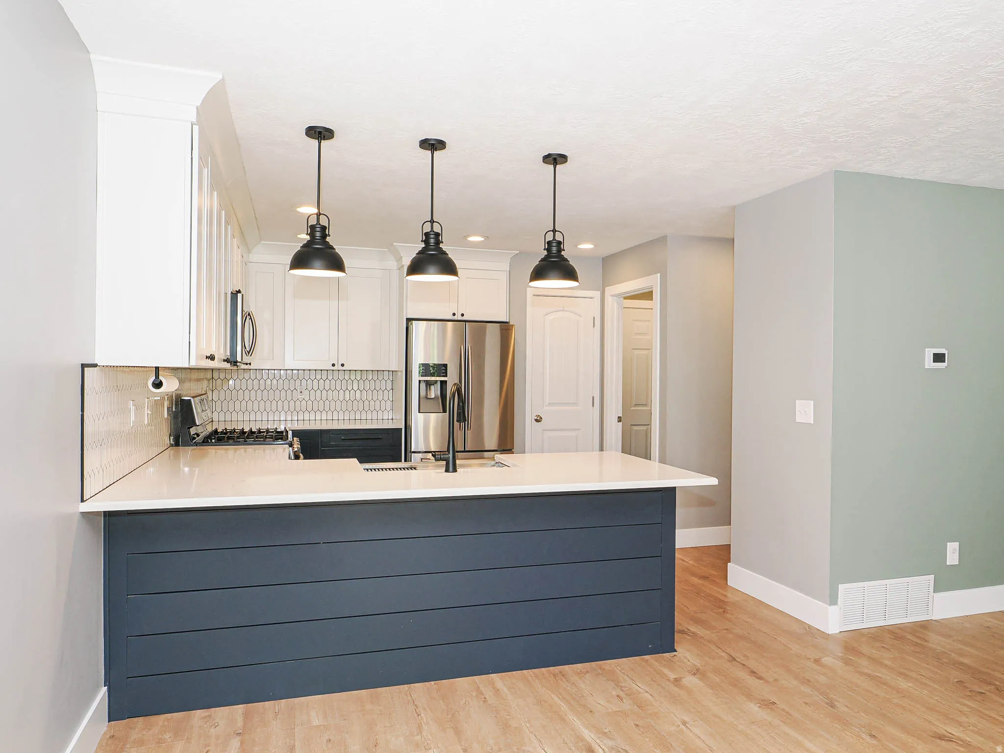 Kitchen island with shiplap-style paneling, pendant lighting, stainless steel appliances, and a tiled backsplash