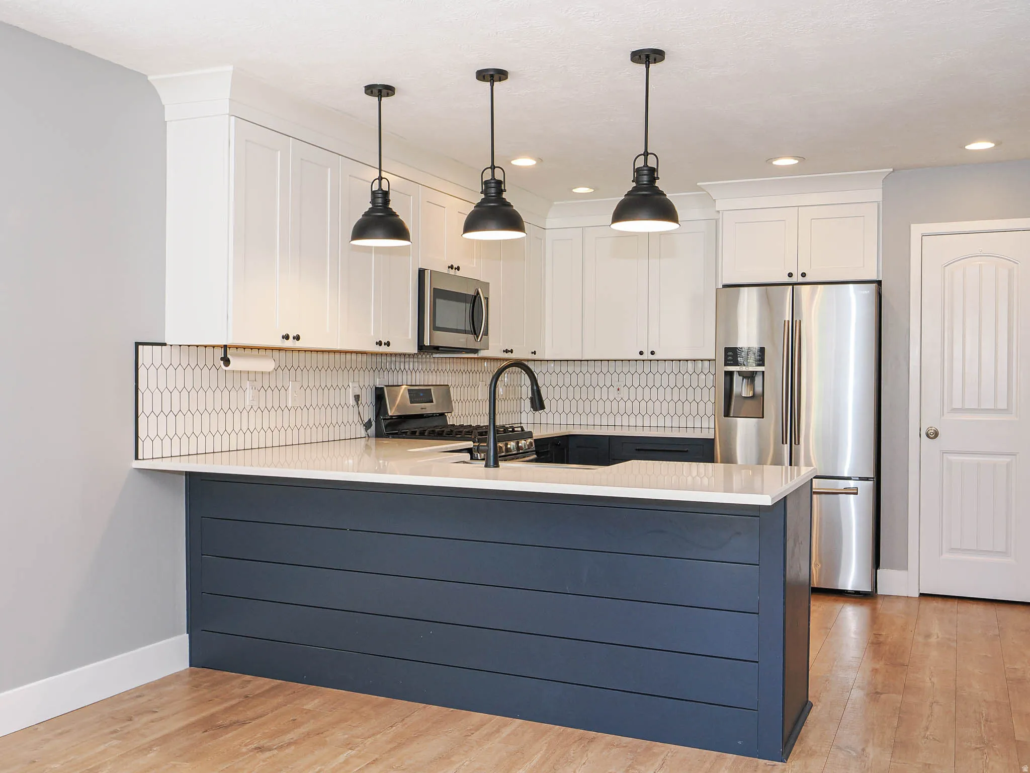 Modern kitchen featuring white shaker cabinetry, stainless steel appliances, a tiled backsplash, wood-finish flooring, and a central island with counter seating