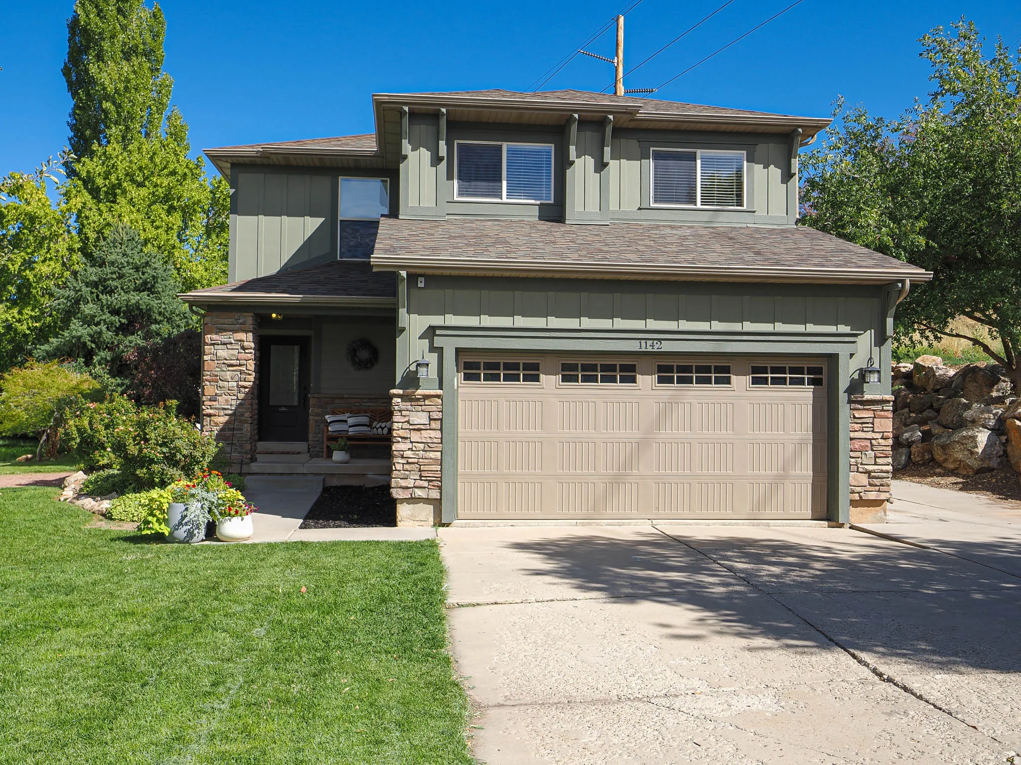 Two-story exterior with board and batten siding, stone accents, asphalt shingle roof, and a two-car garage