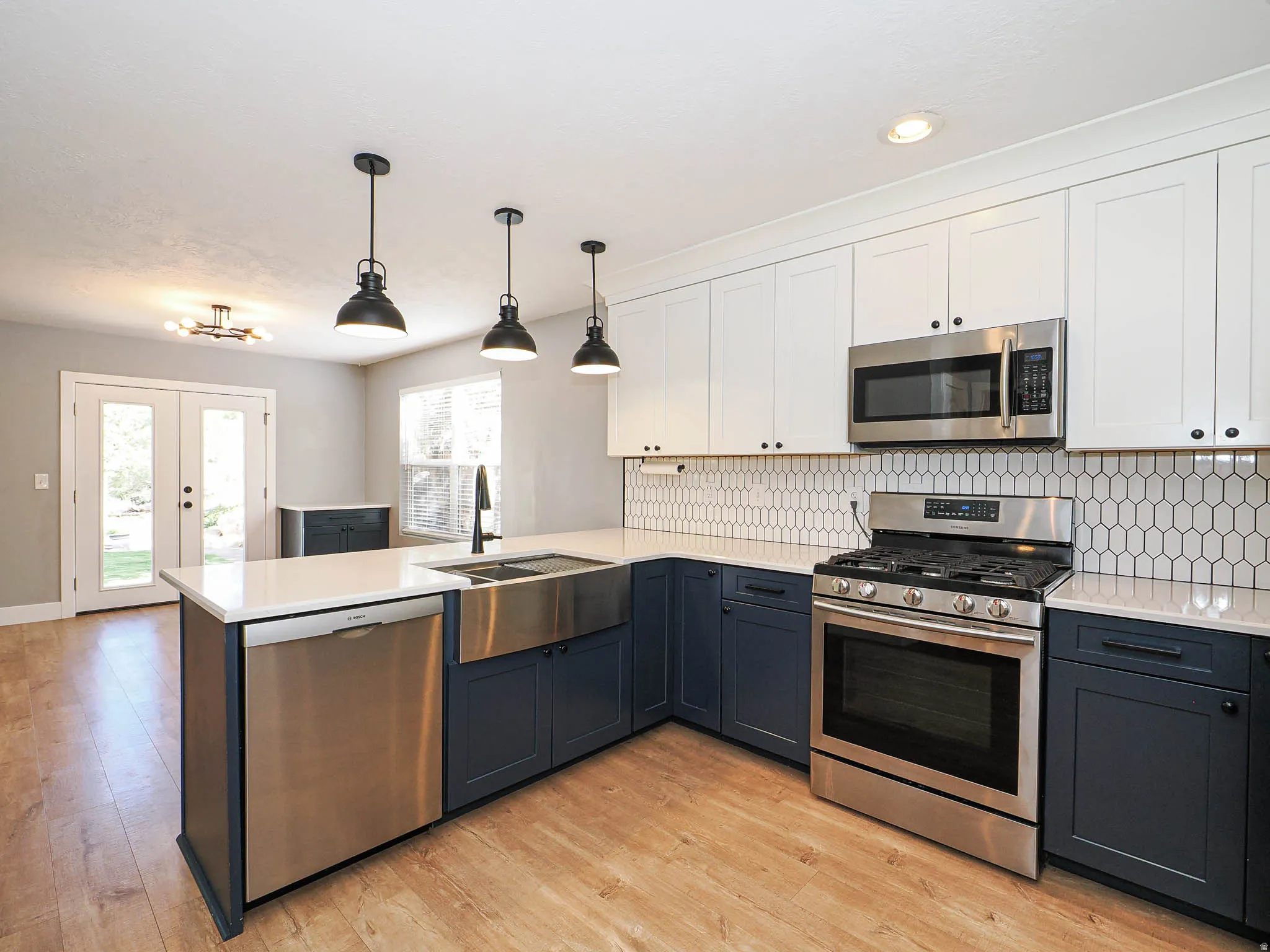 Kitchen featuring wood-finish flooring, two-tone cabinetry, stainless steel appliances, a farmhouse sink, and a hexagonal tile backsplash