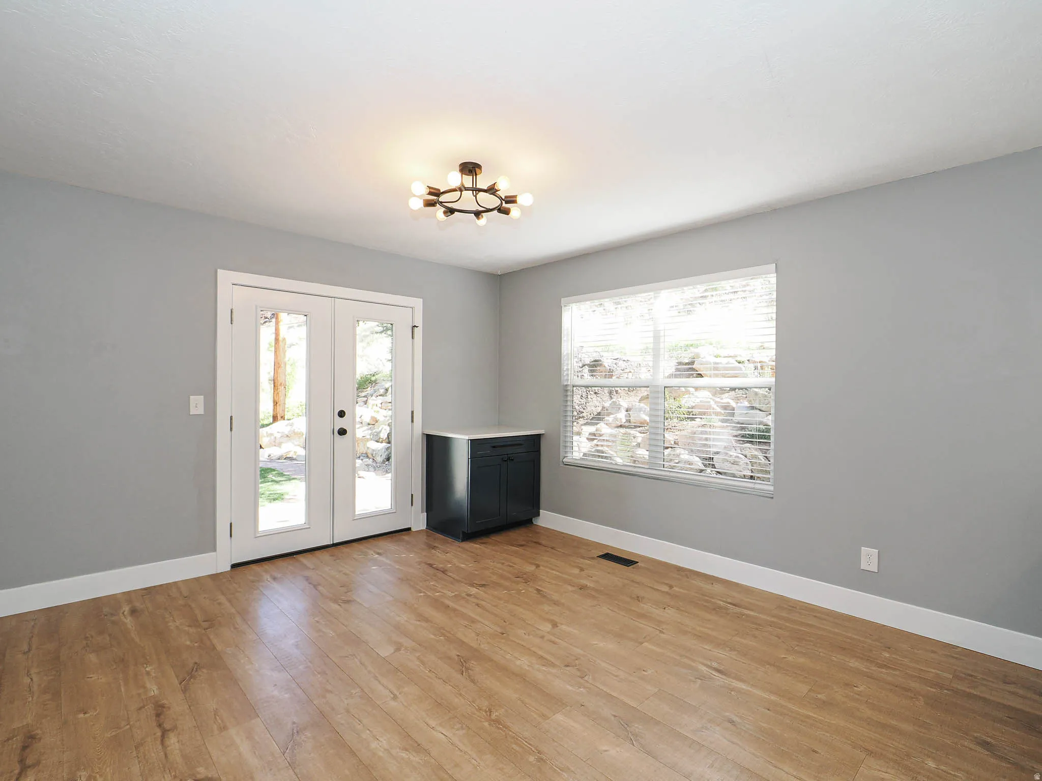 Wood-finish flooring, white trim, dual-pane window with blinds, and white French doors with glass panels
