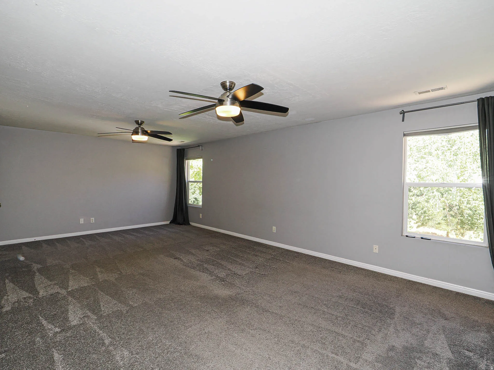 Spacious room featuring gray walls, gray patterned carpeting, and two ceiling fans with integrated lighting