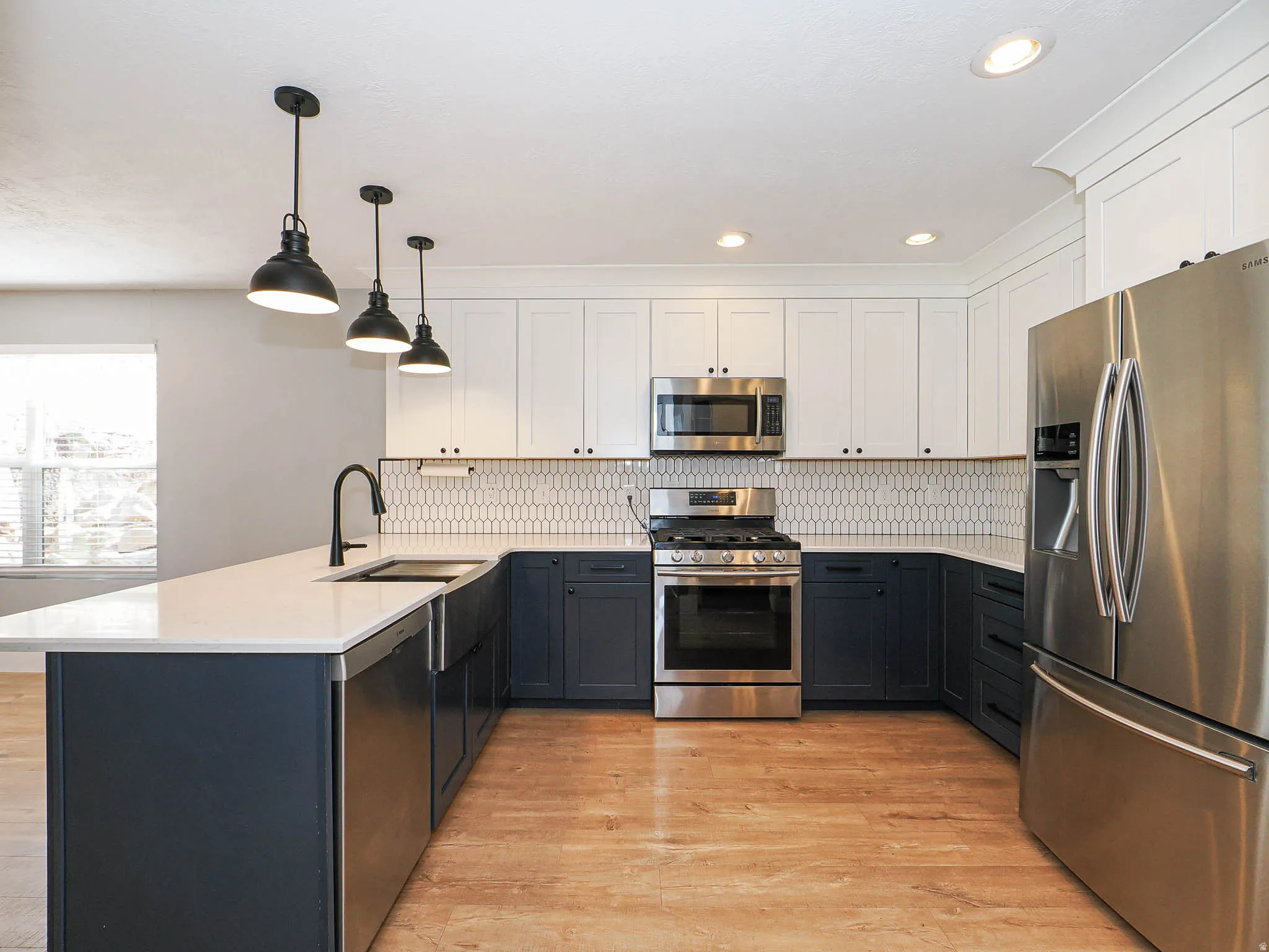Kitchen featuring two-tone cabinetry, stainless steel appliances, a center island with sink, pendant lighting, and wood-finish flooring