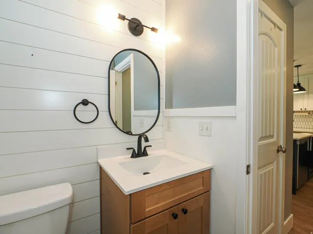 White shiplap wall accentuating the vanity with a black matte faucet, oval mirror, and a modern light fixture