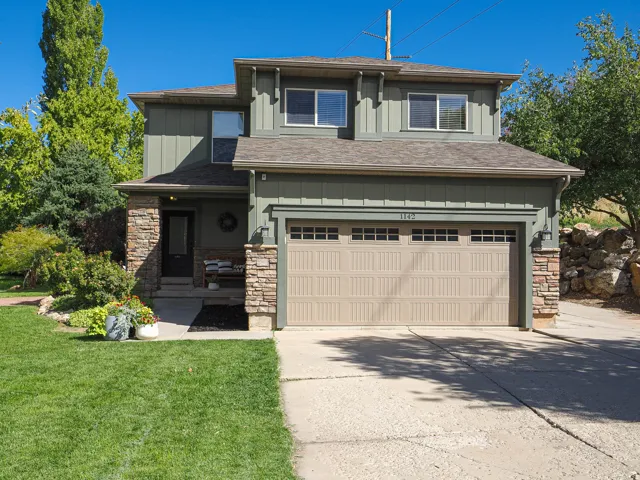 Two-story exterior with board and batten siding, stone accents, asphalt shingle roof, and a two-car garage