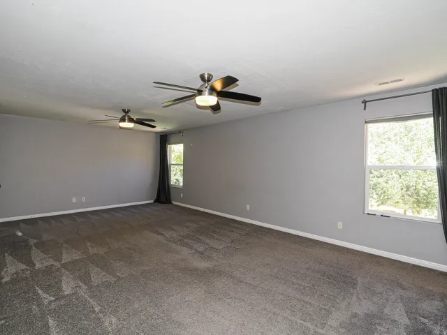 Spacious room featuring gray walls, gray patterned carpeting, and two ceiling fans with integrated lighting