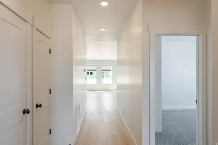 Hallway with wood-finish flooring, recessed lighting, and white paneled doors with black hardware
