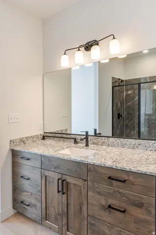 Dual vanity with granite countertop, integrated sink, dark wood-finish cabinetry, and matte black fixtures