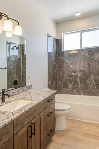 Wood-finish flooring, a vanity with a light-toned countertop, a built-in tub with dark tiled surround, and a rectangular window