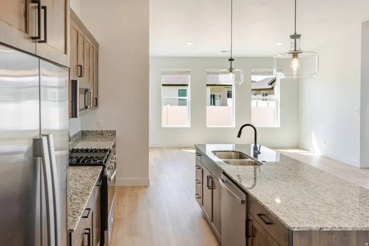 Kitchen featuring wood-finish cabinetry, stainless steel appliances, speckled stone countertops, a double basin sink with a gooseneck faucet, and pendant lighting