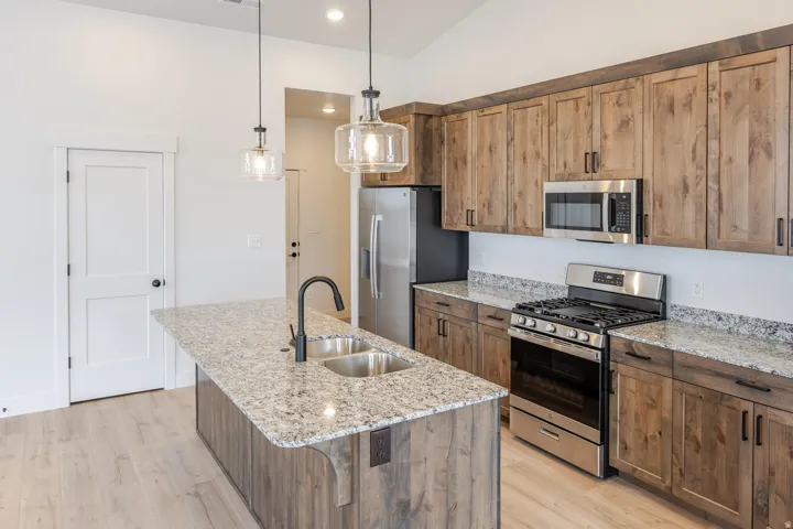 Kitchen featuring light wood-finish flooring, a double basin undermount sink with a matte black faucet, granite countertops, and stainless steel appliances