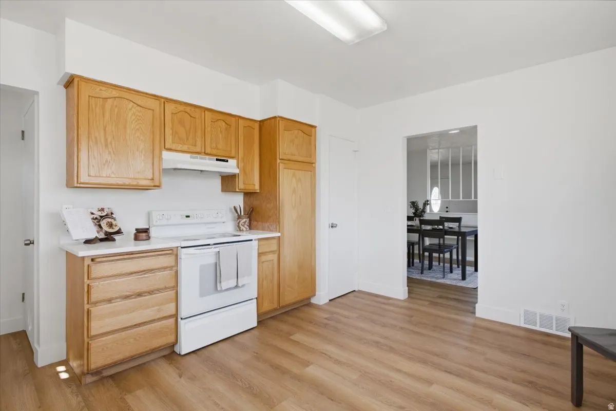 Kitchen featuring wood cabinetry, white countertops, a white range with a range hood, and wood-finish flooring
