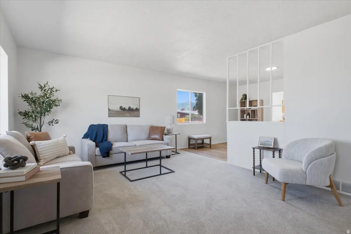 Vaulted ceiling, recessed lighting, expansive carpeted flooring, wood-finish flooring, and a decorative room divider