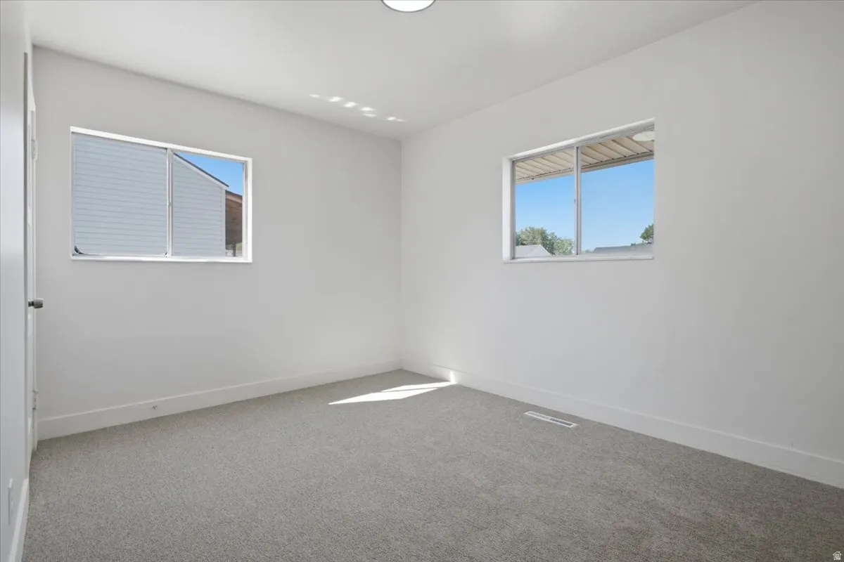 White painted walls, light gray carpeting, and multiple windows