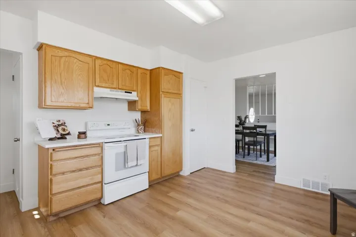 Kitchen featuring wood cabinetry, white countertops, a white range with a range hood, and wood-finish flooring