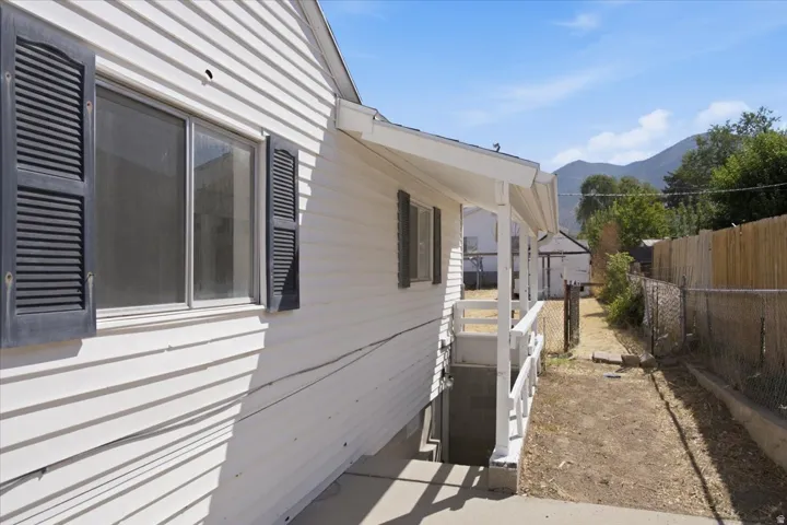 White vinyl siding exterior with dark louvered shutters, covered porch, concrete pathway, and a chain-link fence