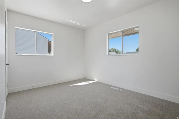 White painted walls, light gray carpeting, and multiple windows