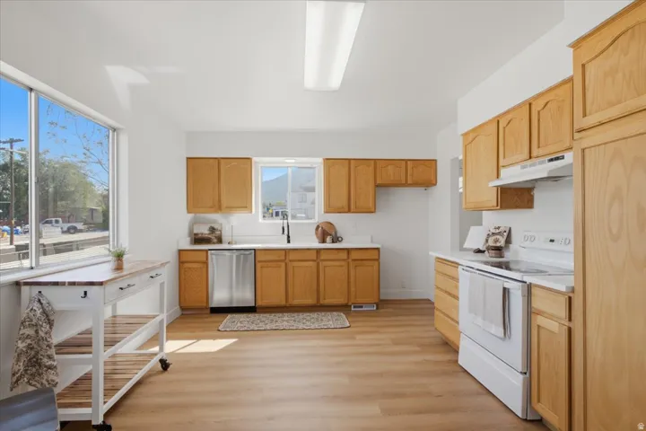 Kitchen featuring wood-finish flooring, light wood cabinetry, white countertops, stainless steel dishwasher, and a white electric range