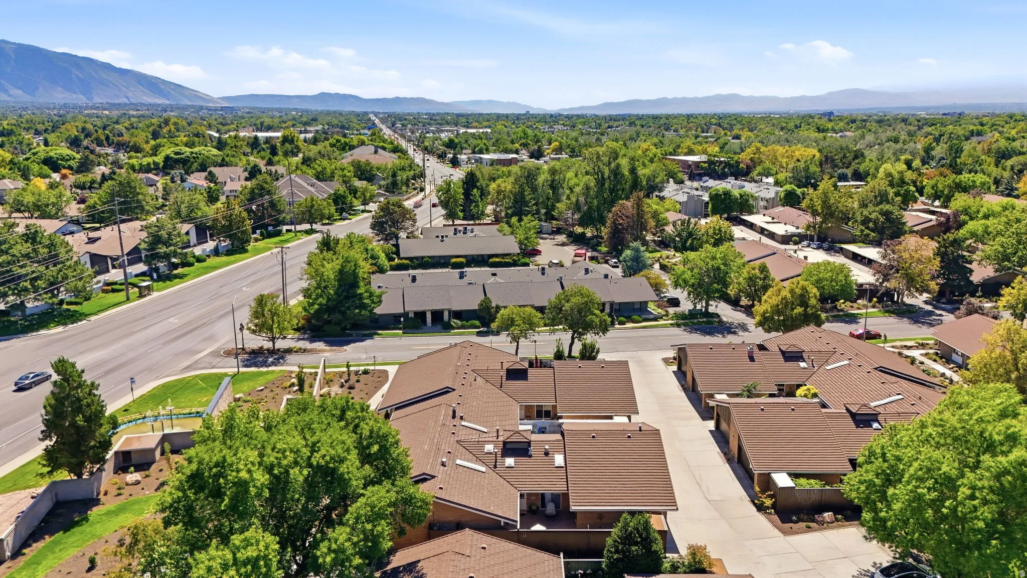 Expansive aerial perspective showcasing multiple residential buildings with brown shingle roofs, surrounded by mature trees