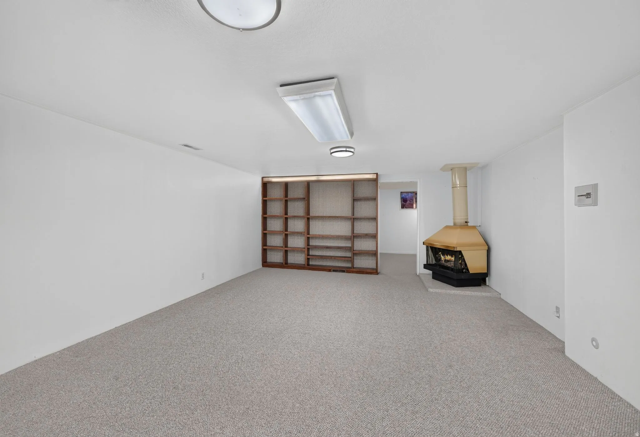 Wall-to-wall carpeting with built-in shelving, a free-standing fireplace, and recessed lighting