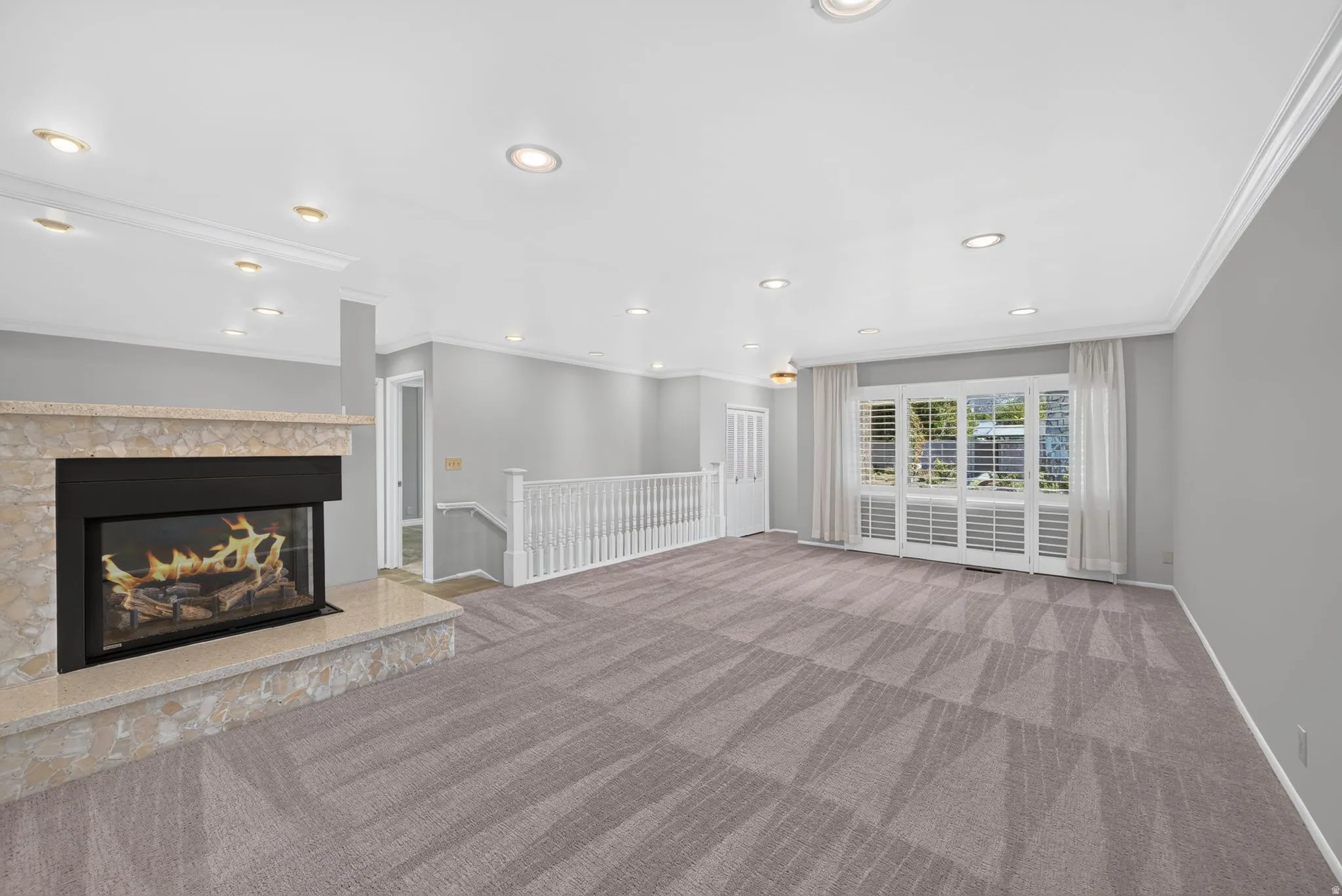 Living area featuring a stone-clad fireplace, patterned carpet, recessed lighting, and crown molding