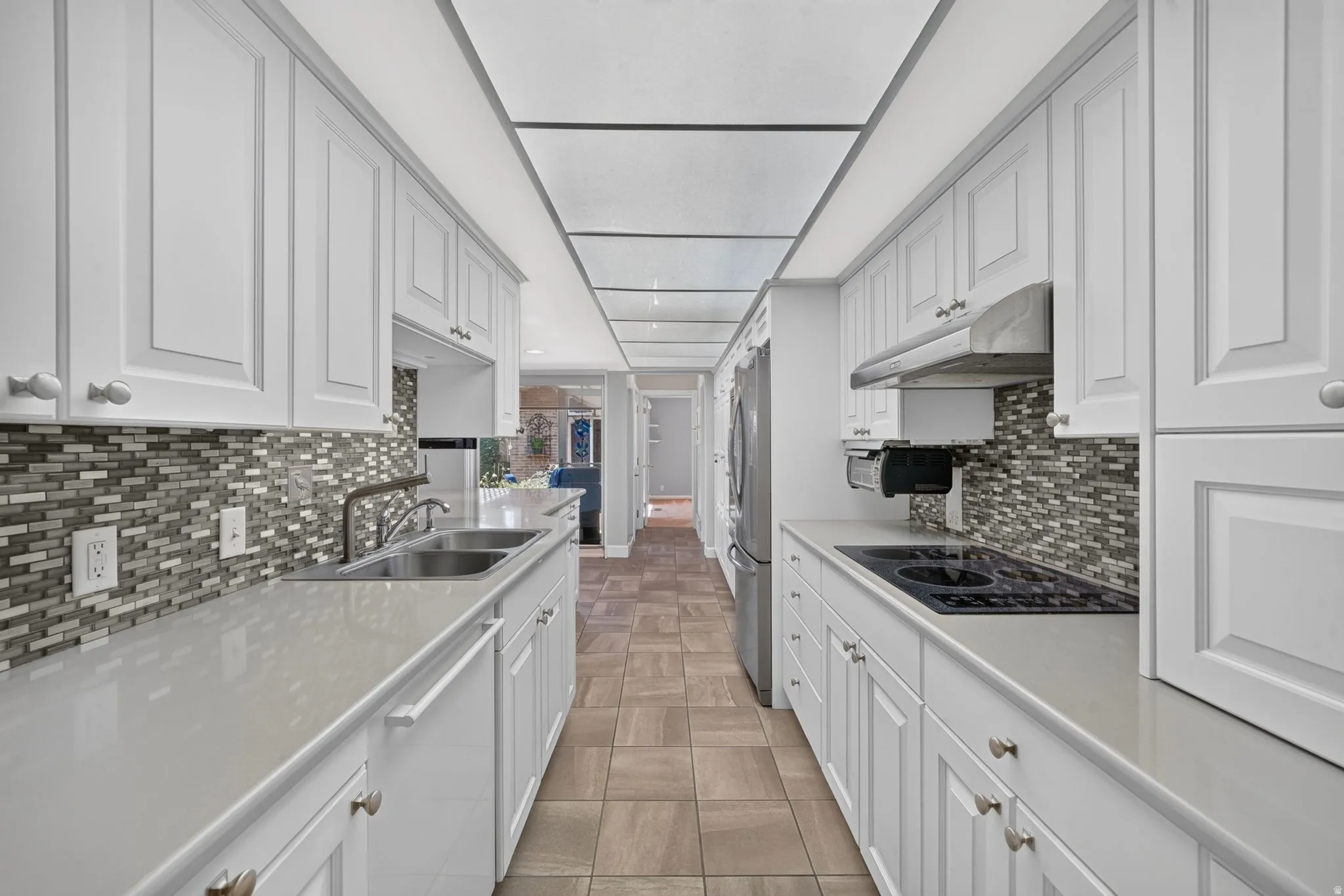 Galley kitchen featuring white cabinetry, light countertops, mosaic tile backsplash, stainless steel appliances, and tile flooring