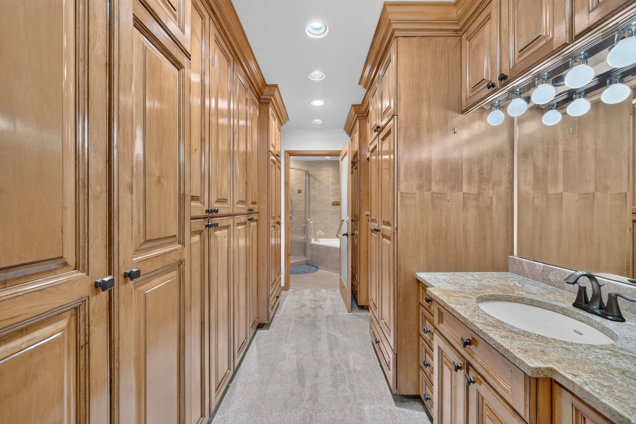 Extensive wood-finish cabinetry with black hardware, built-in vanity with an undermount sink, stone countertop, and large mirror