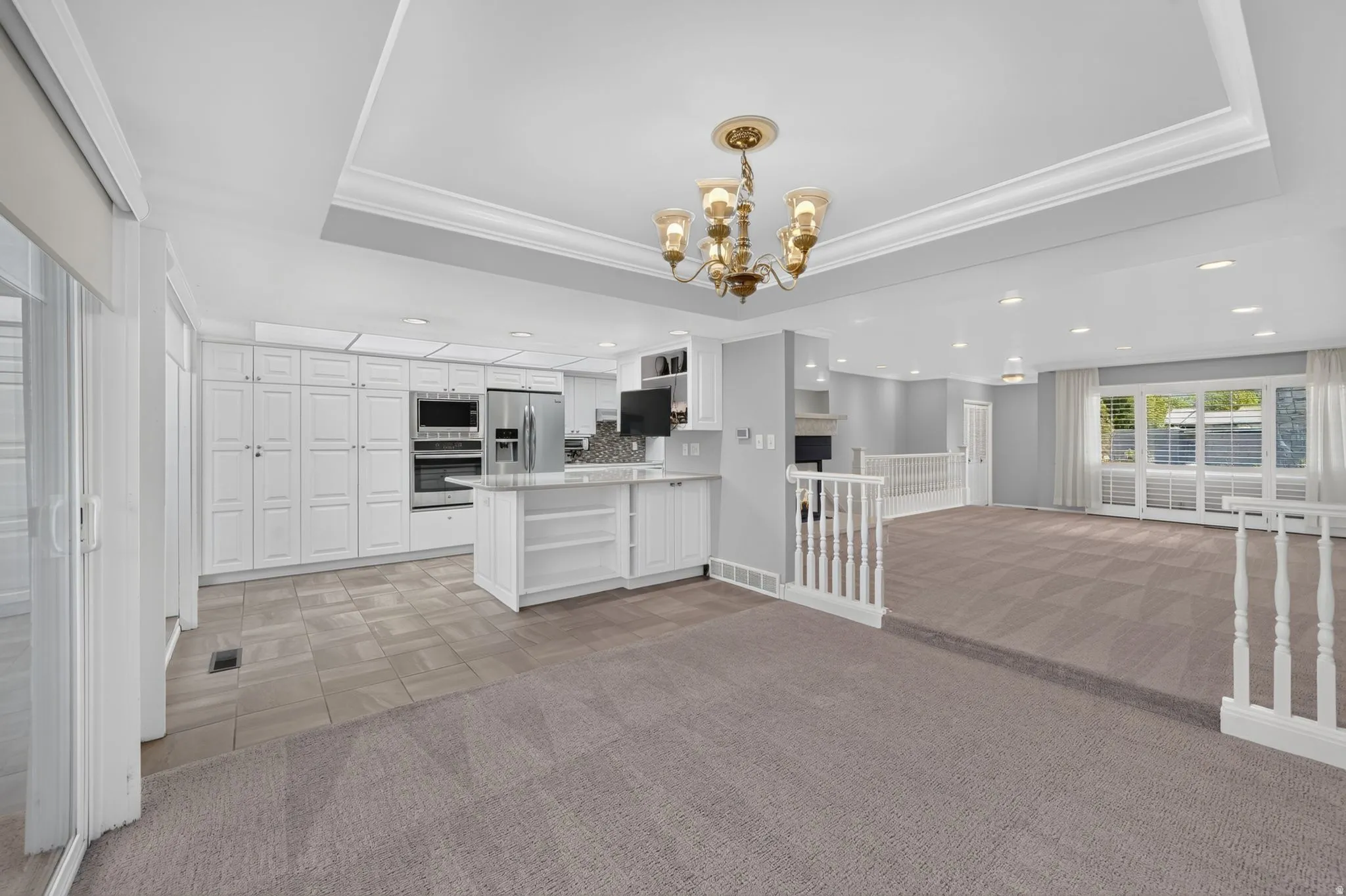 Recessed lighting, large white cabinetry, stainless steel appliances, central island with seating, and a decorative chandelier