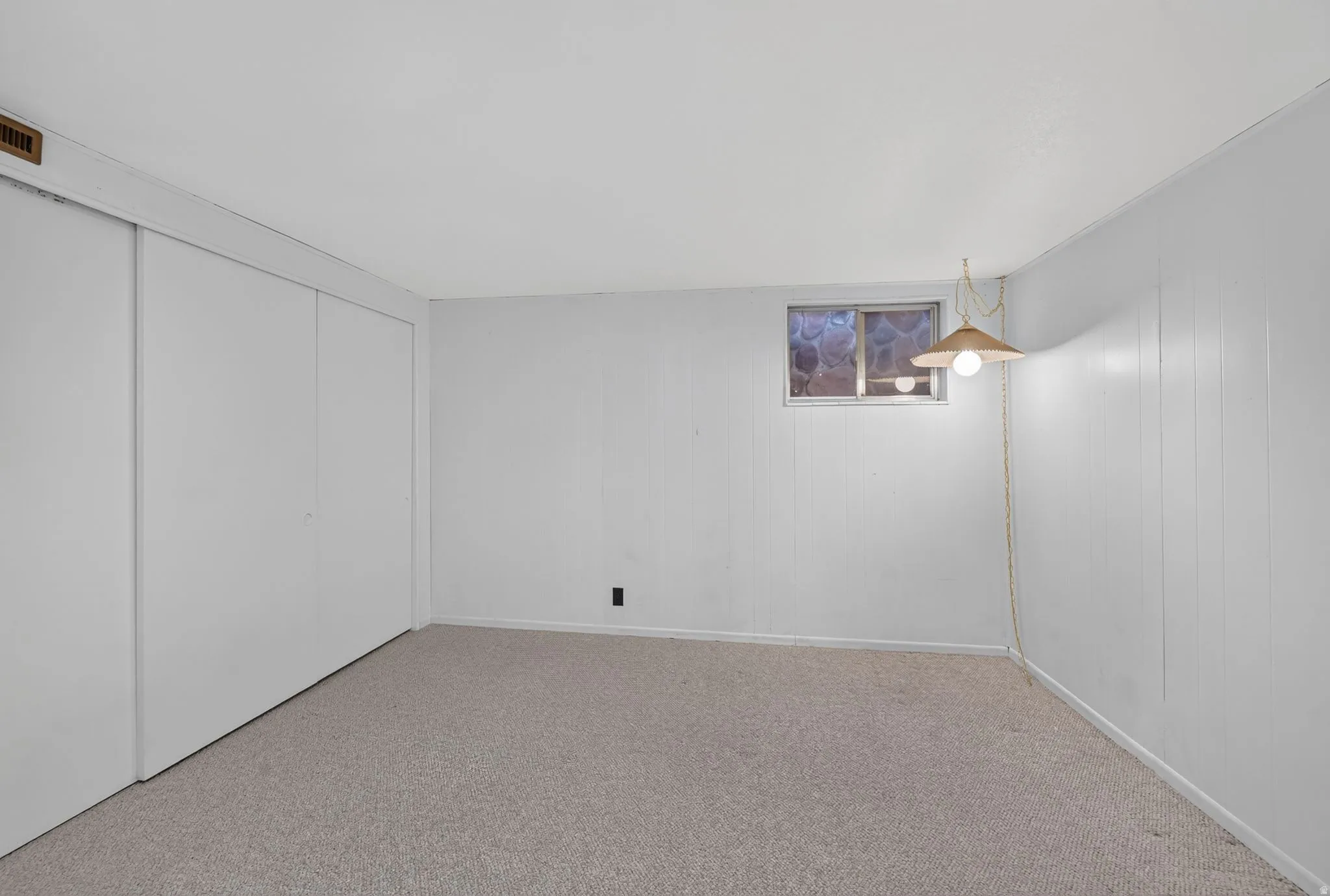 Wall-to-wall carpeting, white paneled walls, and a single window