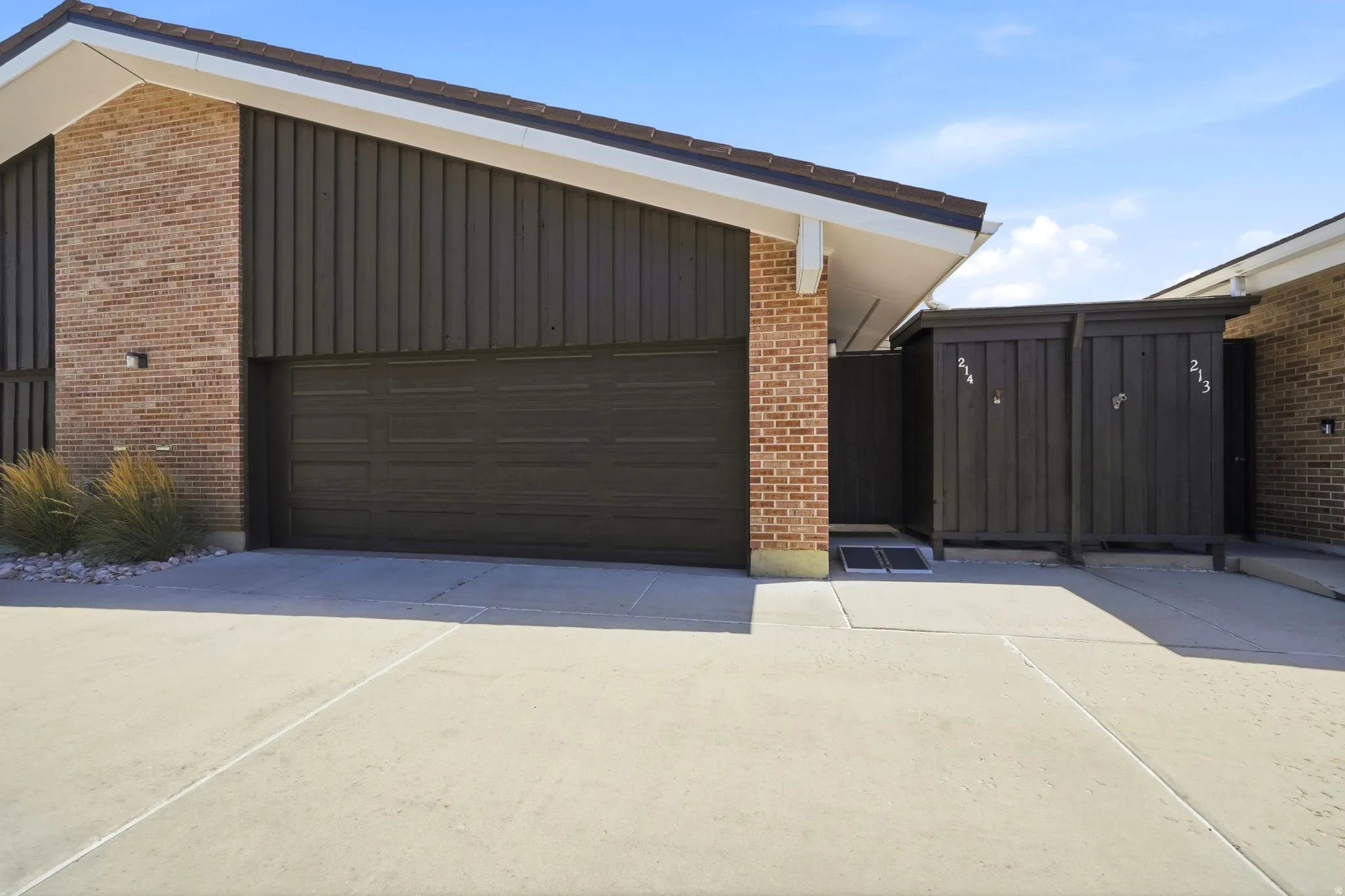 Brick facade with vertical paneling, attached garage, and a concrete driveway